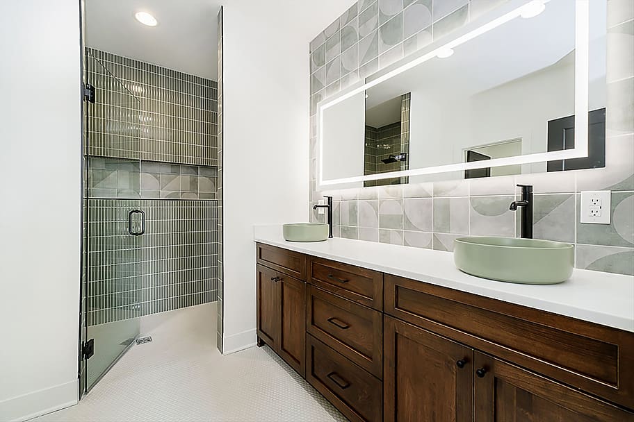 Primary Bathroom with Green Tile Shower, Double Sink, Illuminated Mirror, and Green Backsplash