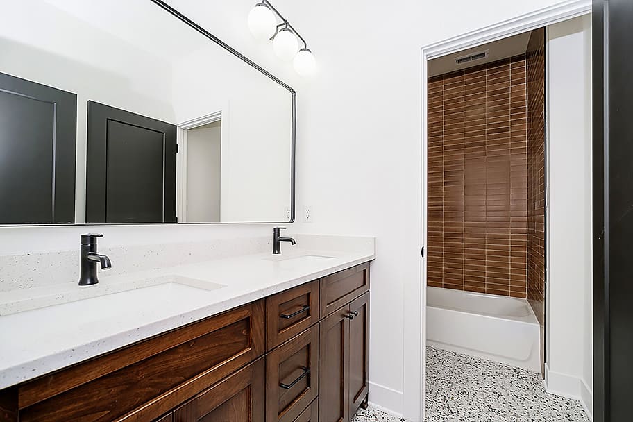 Guest Bathroom with Brown Tile Shower and Double Vanity with Black Accents by Gem Homes Indianapolis