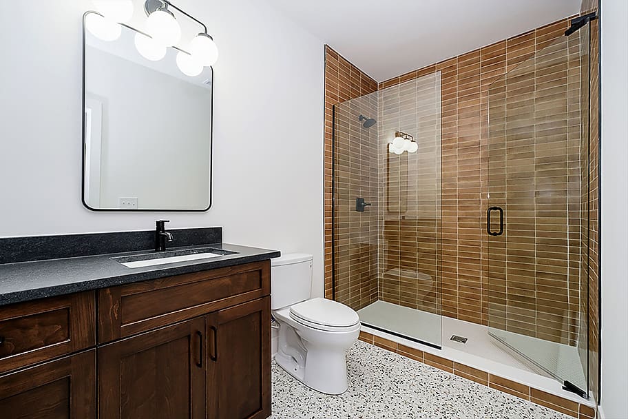Guest Bathroom with Brown Tile, Glass Shower Door, Double Vanity, and Black Accents