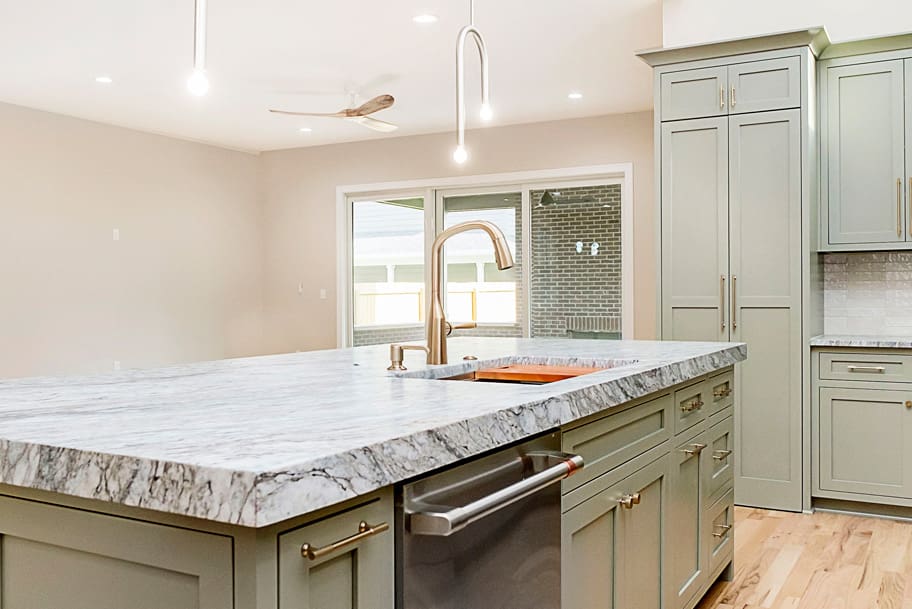 Close-Up of Kitchen Island with Green Cabinets, Granite Countertop, and Gold Accents on Sink and Drawer Pulls