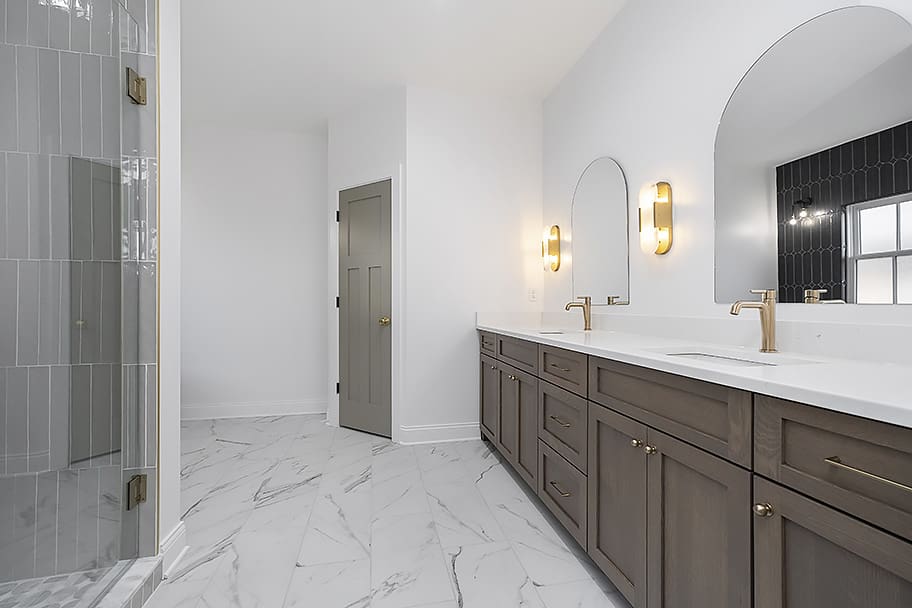 Long Primary Bathroom with Double Sinks, Arched Individual Mirrors, and Gray and White Marble Flooring in a Custom Home by Gem Homes Indianapolis