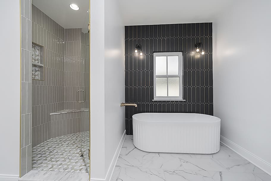 Primary Bathroom with Pinky Beige Vertical Tile Wall, Patterned Shower Floor, Glass Door, and Soaking Tub with Black Tile Wall in a Custom Home by Gem Homes Indianapolis
