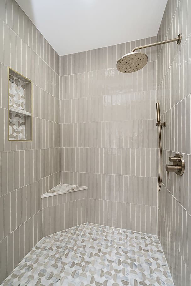 Shower with Beige Vertical Tiles, Patterned Floor, Glass Door, and Gold Round Shower Head in Custom Bathroom by Gem Homes Indianapolis